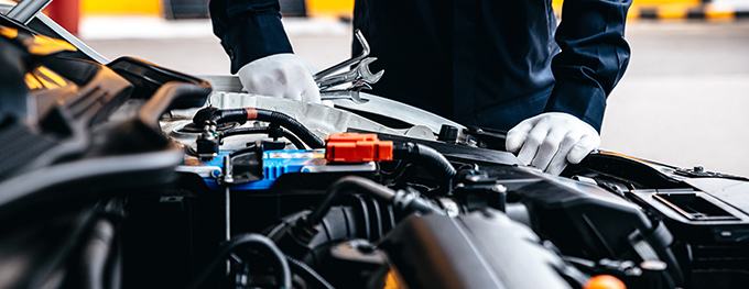 a mechanic holding spanners in white gloves looking at the engine under the bonnet of a car